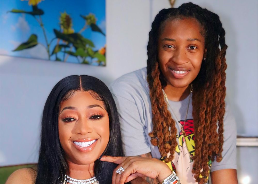 visual storytelling for brand transformation. Smiling women posing together indoors, with one wearing a white outfit and the other in a graphic t-shirt with long locs, against a backdrop of bright flowers and art.